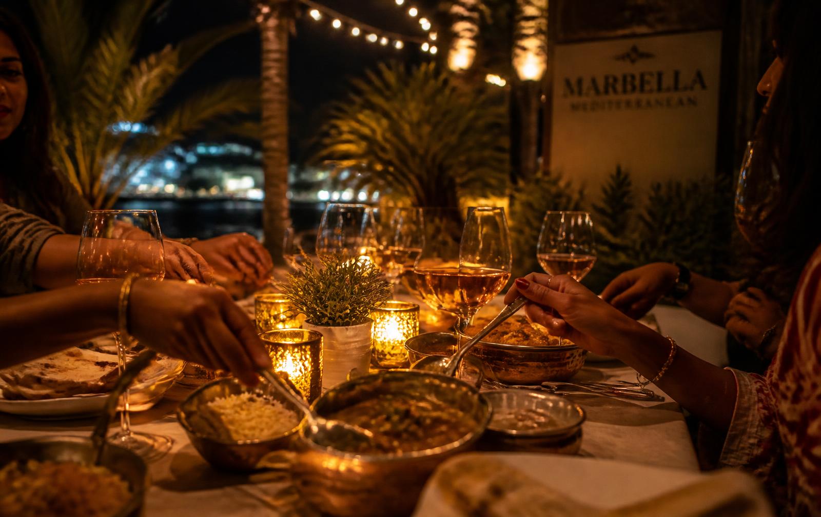 Group sharing Indian curries and naan on a candle-lit Marbella terrace at night